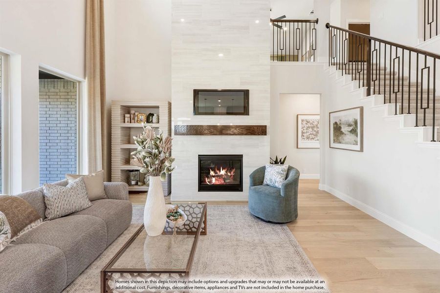 Open living room with two-story ceiling, tile fireplace, hardwood floors, and staircase with metal railing