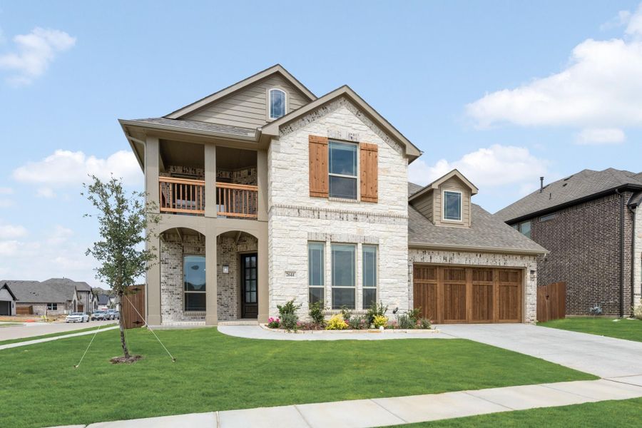 Two-story home with stone and brick exterior, second-floor balcony, wood shutters, and two-car garage