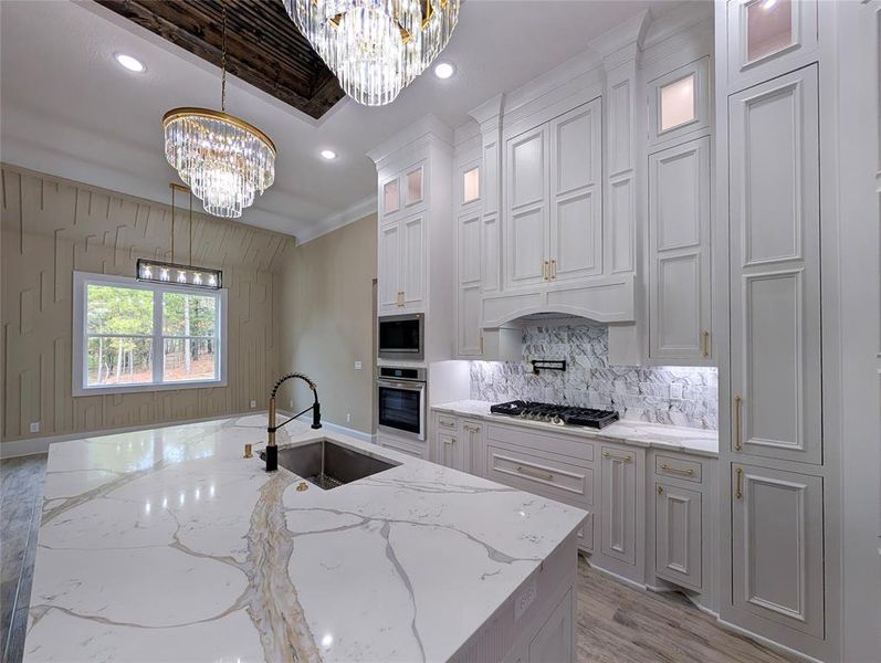 Kitchen with light stone counters, pendant lighting, glass insert cabinets, ornamental molding, and stainless steel appliances