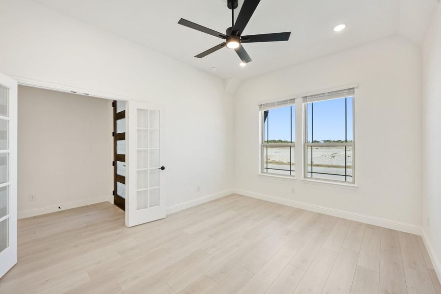 Empty bedroom with light wood floors, black ceiling fan, and French doors leading to closet Empty bedroom with light wood floors, black ceiling fan, and French doors leading to closet