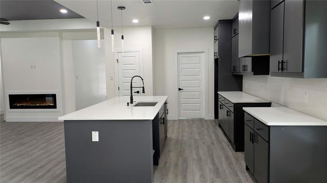 Kitchen featuring light countertops, a center island with sink, a sink, and light wood finished floors