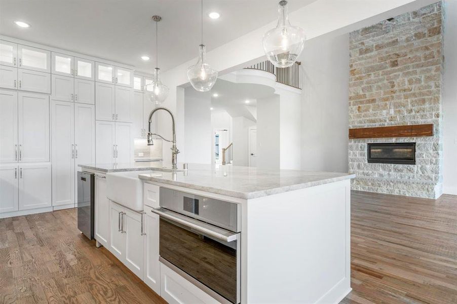 Kitchen featuring white cabinetry, a center island with sink, stainless steel oven, and pendant lighting