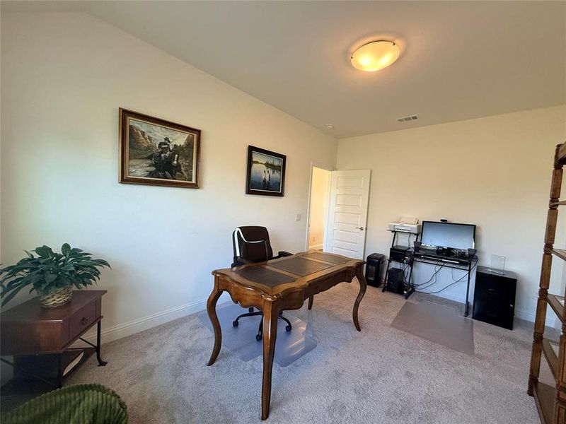 Carpeted room with high ceilings, featuring a five-panel interior door, and a flush-mount ceiling light fixture Carpeted room with high ceilings, featuring a five-panel interior door, and a flush-mount ceiling light fixture