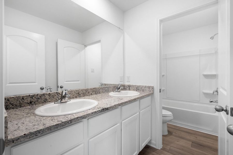 Bathroom with double vanity, dark wood-style floors, and shower / tub combination