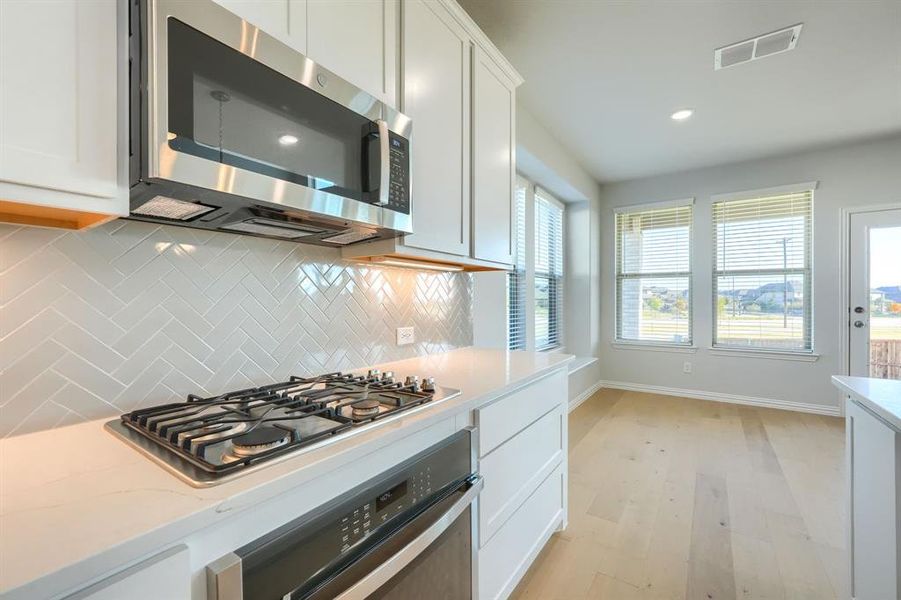 Kitchen with decorative backsplash, stainless steel appliances, white cabinets, light wood-style flooring, and recessed lighting Kitchen with decorative backsplash, stainless steel appliances, white cabinets, light wood-style flooring, and recessed lighting