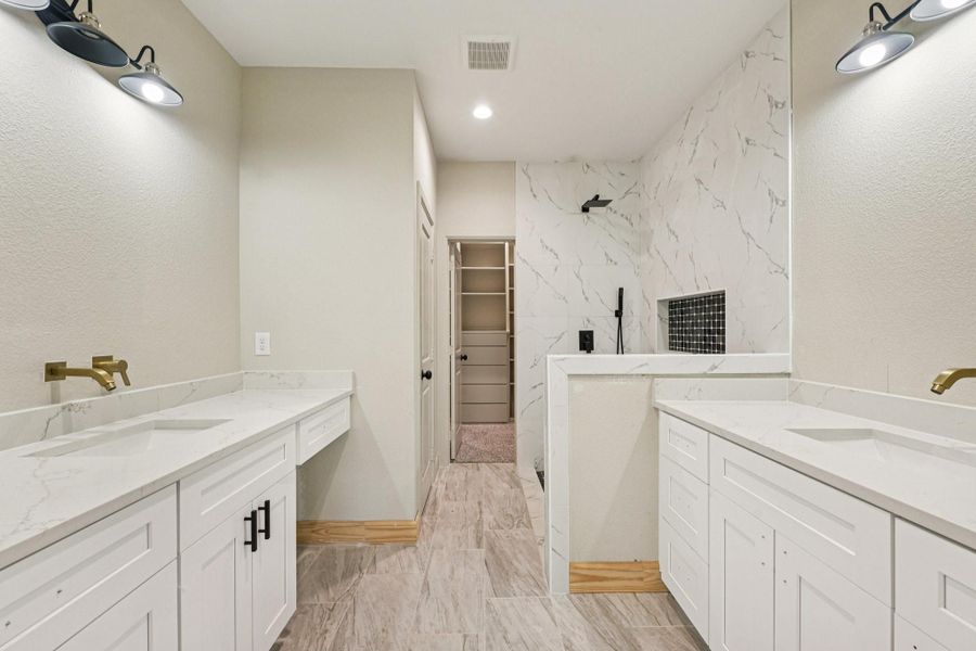 This modern bathroom features dual sinks with white cabinetry and Quartz countertops. It has a spacious walk-in shower with elegant tile work and a built-in shelf.