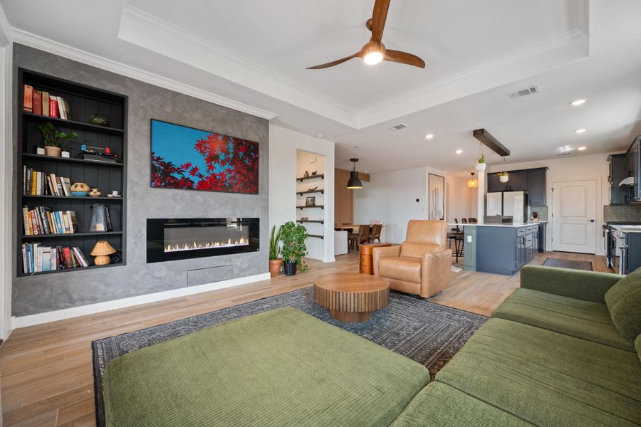 Living area with light wood-style floors, a raised ceiling, built in features, a large fireplace, and ceiling fan Living area with light wood-style floors, a raised ceiling, built in features, a large fireplace, and ceiling fan