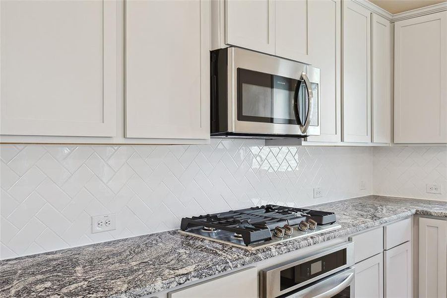 Kitchen featuring tasteful backsplash, appliances with stainless steel finishes, light stone counters, and white cabinetry