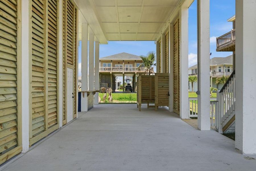 This photo showcases a covered outdoor area with wooden slatted walls, ideal for storage or relaxation. It features a concrete floor and provides a view of neighboring homes and greenery, enhancing the sense of community.