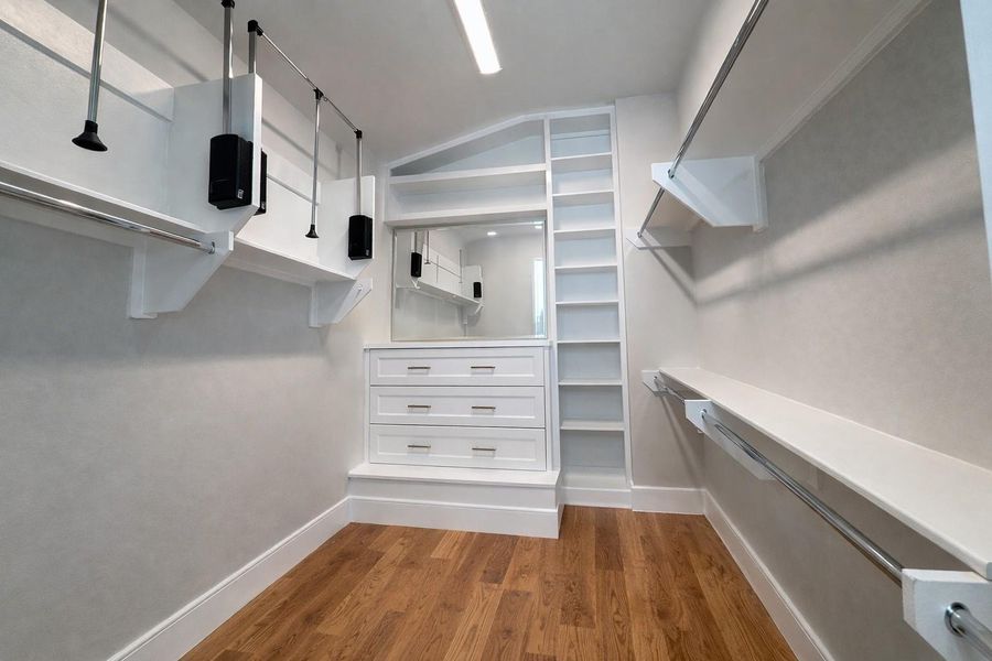 Primary closet with custom built-ins.   Virtually enhanced with wood floors and mirror.