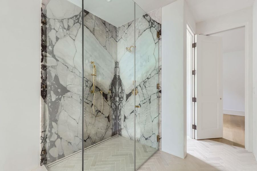 A striking walk-in shower features dramatic veined marble and elegant gold fixtures, adding a touch of grandeur.