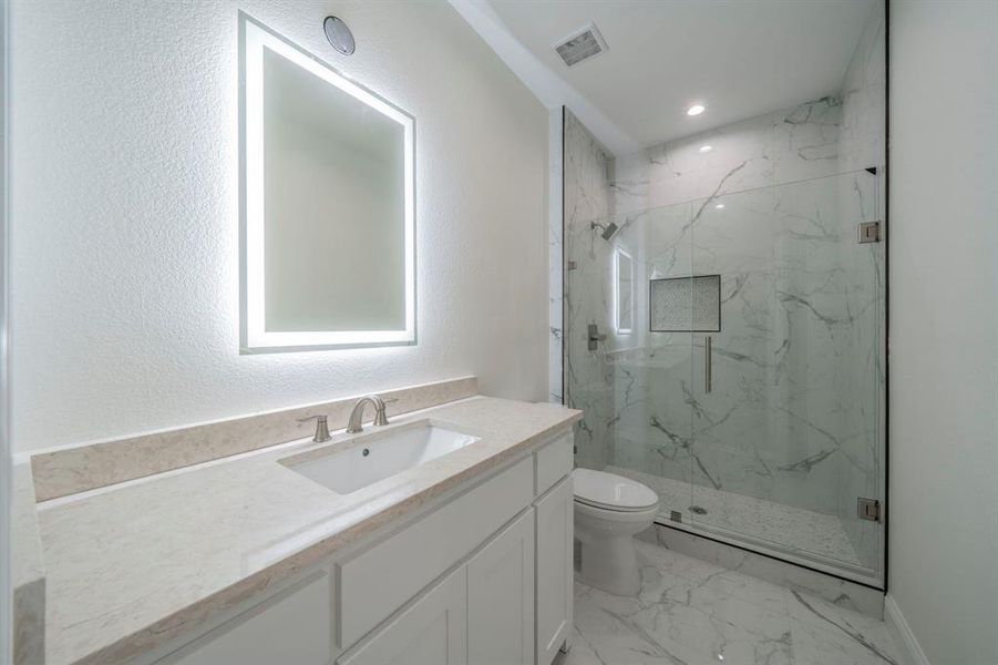 Full bathroom with vanity, a marble finish shower, a textured wall, and light marble finish floors Full bathroom with vanity, a marble finish shower, a textured wall, and light marble finish floors