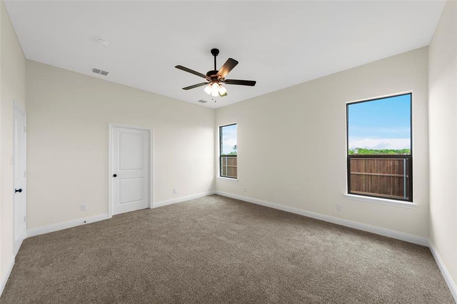 Spacious room featuring vaulted ceilings, neutral-toned carpeting, two windows providing natural light, a ceiling fan with integrated lighting, and white interior doors