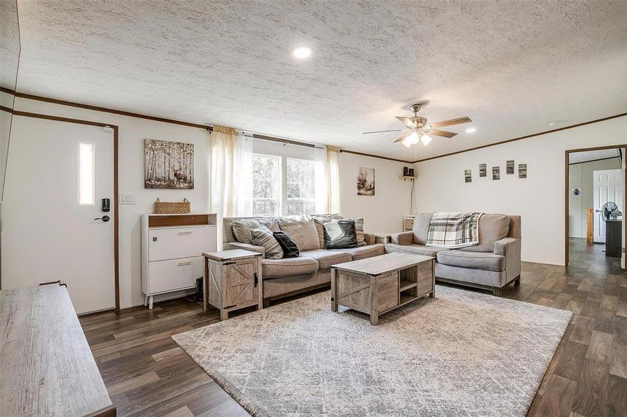 Living room featuring a textured ceiling, dark wood-type flooring, crown molding, and ceiling fan