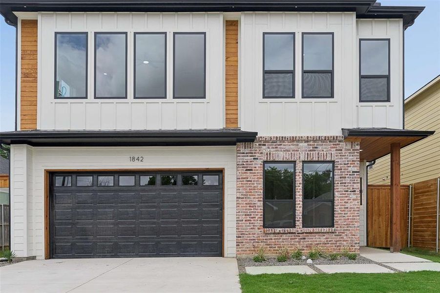 Modern two-story facade with white board and batten siding, contrasting brick accents, and dark-framed windows Modern two-story facade with white board and batten siding, contrasting brick accents, and dark-framed windows