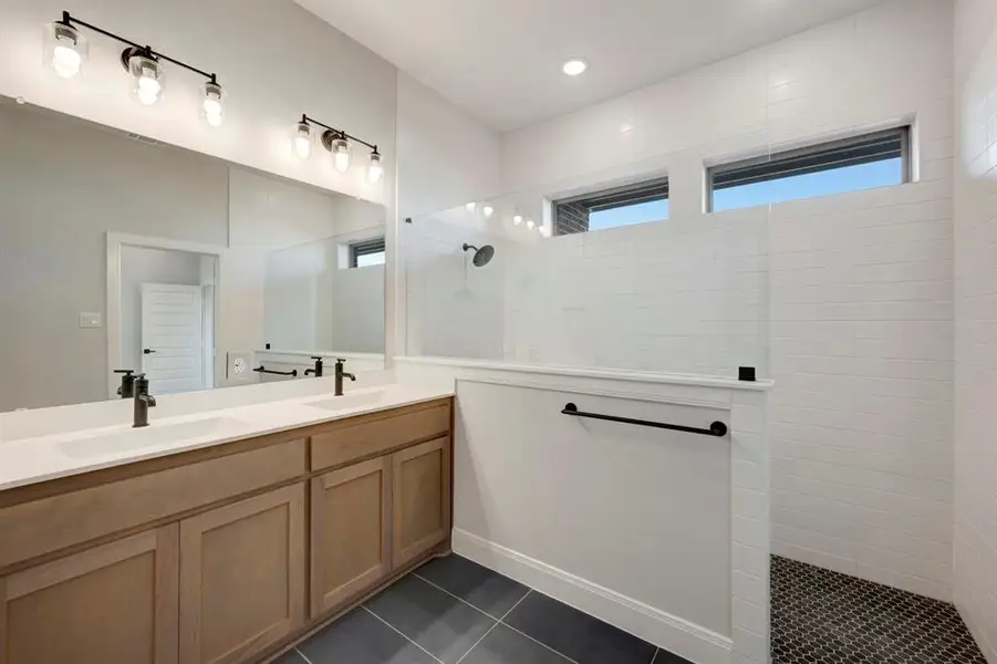 Bathroom with double vanity, a walk in shower, and dark tile patterned floors
