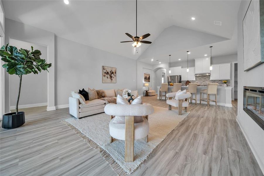 Living room with arched walkways, ceiling fan, light wood-style floors, high vaulted ceiling, and recessed lighting Living room with arched walkways, ceiling fan, light wood-style floors, high vaulted ceiling, and recessed lighting