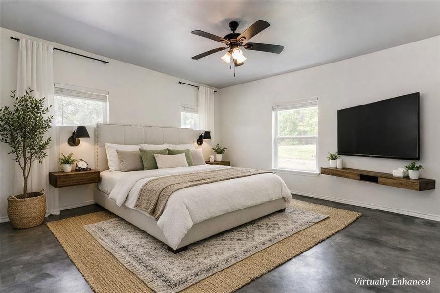 Spacious room featuring a light-colored upholstered bed frame, two windows with white blinds, dark wood-finish flooring, a ceiling fan with integrated lighting, and a wall-mounted wood-finish console