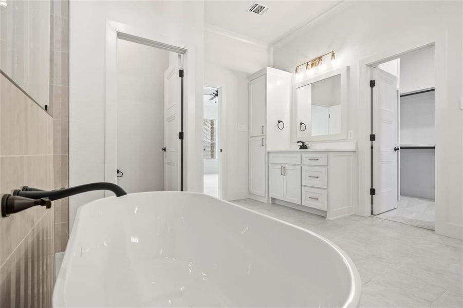 Full bathroom featuring a freestanding bath, vanity, ornamental molding, light tile patterned flooring, and a spacious closet