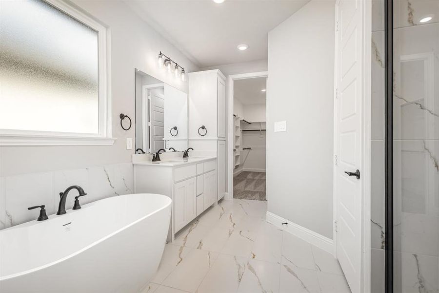Bathroom featuring double vanity, a freestanding tub, a spacious closet, recessed lighting, and light marble finish flooring