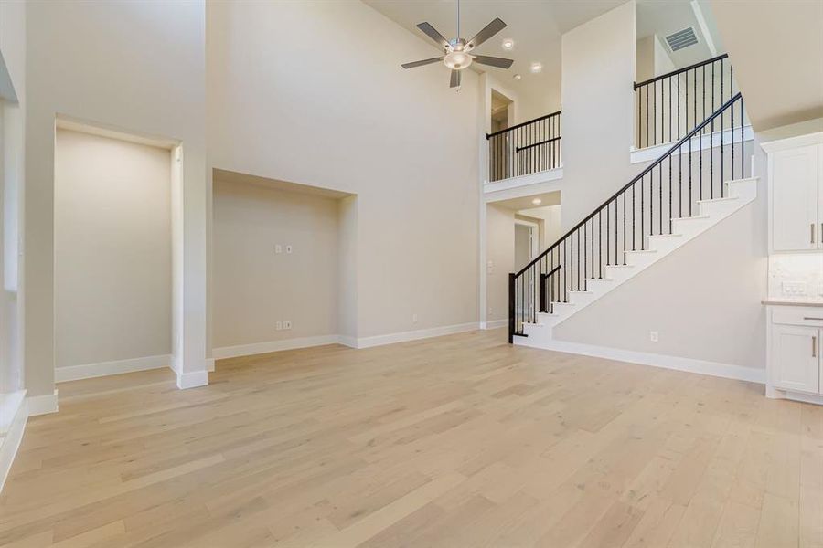 Unfurnished living room featuring light wood-style flooring, a towering ceiling, stairs, and a ceiling fan