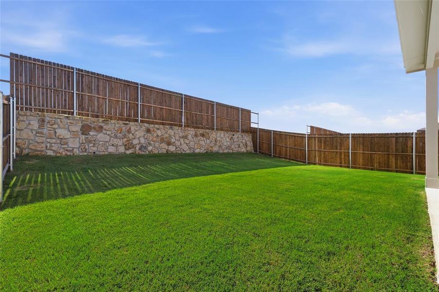 Expansive backyard featuring a manicured lawn, a stone retaining wall, and a full perimeter wood privacy fence