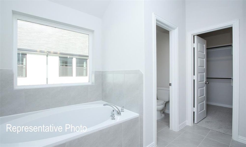 Bathroom with tiled bath, tile patterned floors, toilet, and a healthy amount of sunlight