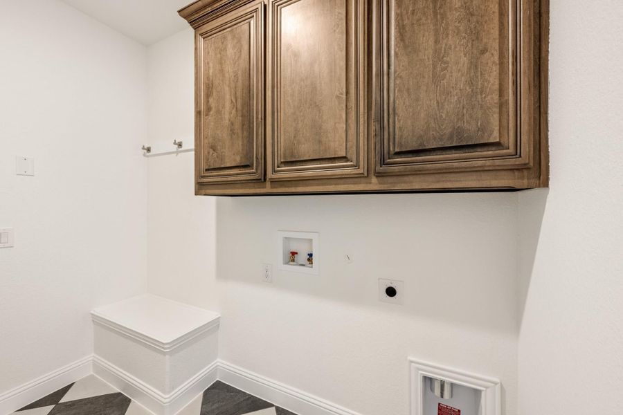 Laundry room with dark wood upper cabinets, washer hookups, and tile floor Laundry room with dark wood upper cabinets, washer hookups, and tile floor