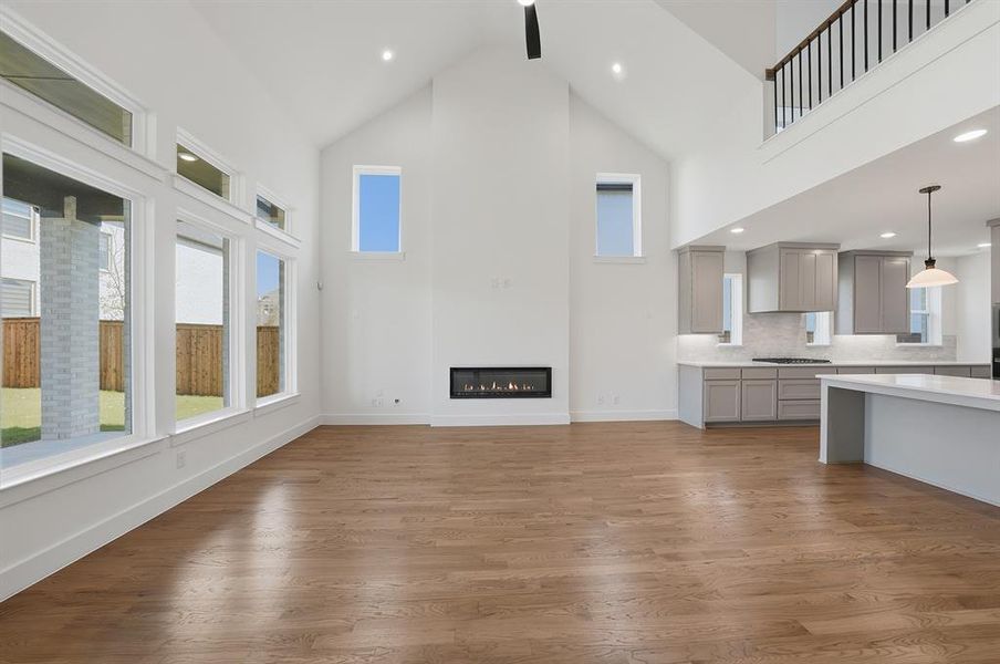 Unfurnished living room featuring high vaulted ceiling, plenty of natural light, dark wood-type flooring, a glass covered fireplace, and recessed lighting Unfurnished living room featuring high vaulted ceiling, plenty of natural light, dark wood-type flooring, a glass covered fireplace, and recessed lighting