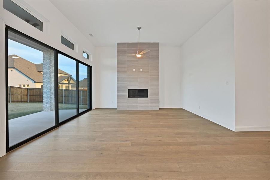 Living room with a tiled fireplace, ceiling fan, and light hardwood / wood-style flooring