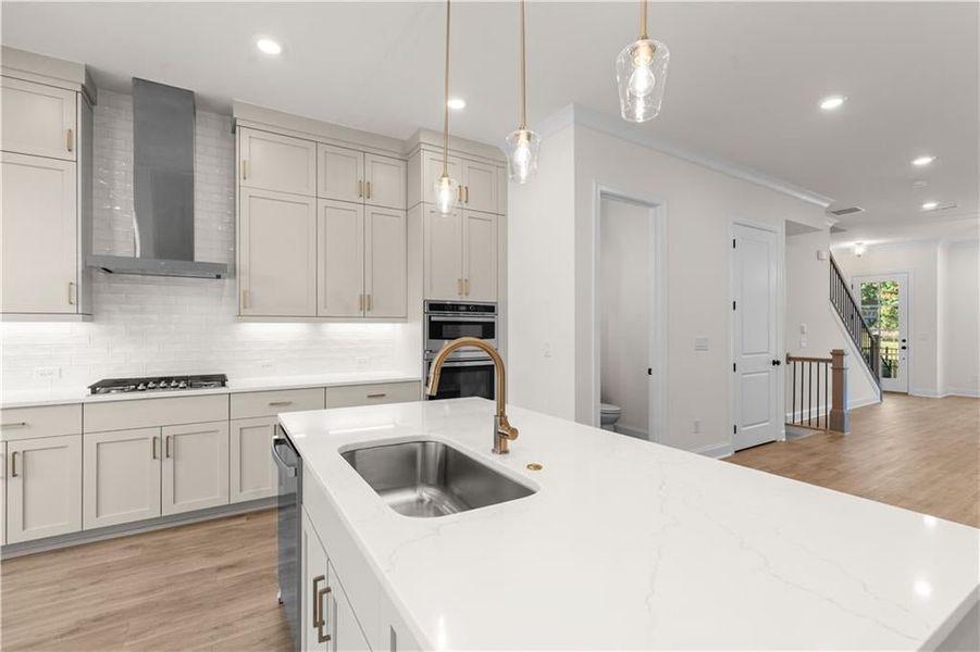 Kitchen featuring light wood finished floors, light stone countertops, backsplash, recessed lighting, and wall chimney range hood