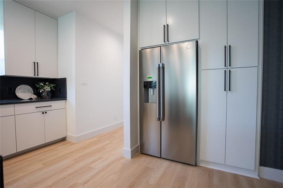 Kitchen with stainless steel fridge with ice dispenser, light wood-type flooring, and white cabinetry