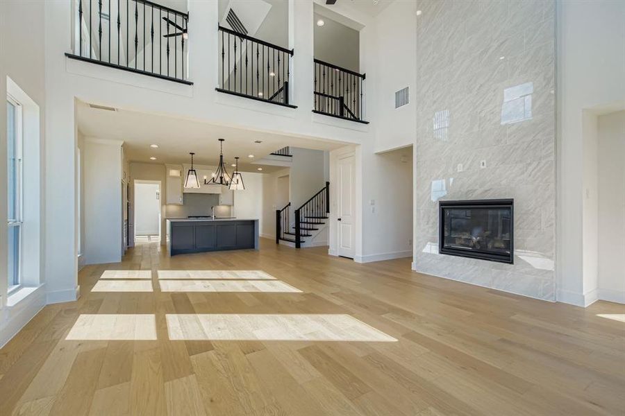 Unfurnished living room with a tiled fireplace, light wood-type flooring, stairway, a high ceiling, and recessed lighting Unfurnished living room with a tiled fireplace, light wood-type flooring, stairway, a high ceiling, and recessed lighting