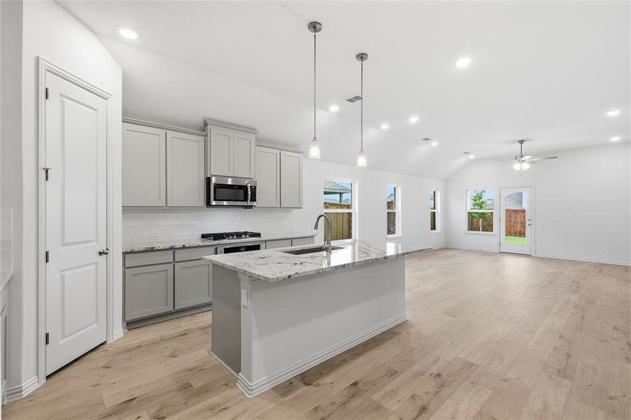 Open-concept kitchen featuring an island with a sink, pendant lighting, stainless steel appliances, and light-toned cabinetry Open-concept kitchen featuring an island with a sink, pendant lighting, stainless steel appliances, and light-toned cabinetry