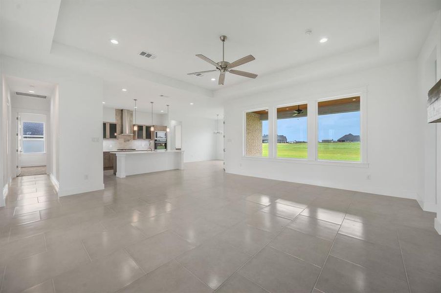 Unfurnished living room with light tile patterned floors, ceiling fan, a tray ceiling, and visible vents Unfurnished living room with light tile patterned floors, ceiling fan, a tray ceiling, and visible vents