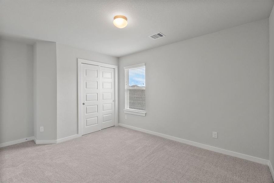 Elegance meets functionality in the generously sized secondary bedrooms, showcasing 5-panel doors with modern hardware, large windows adorned with privacy blinds, and spacious closets boasting sleek and contemporary finishes. Sample photo of completed home with similar floor plan. As-built interior colors and selections may vary.