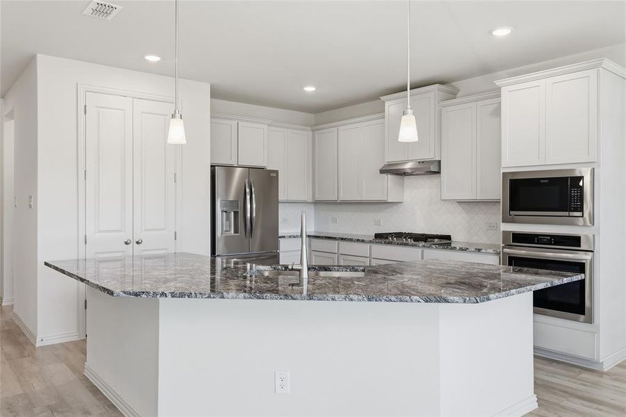 Kitchen featuring light wood-style floors, stainless steel appliances, a kitchen island with sink, and backsplash Kitchen featuring light wood-style floors, stainless steel appliances, a kitchen island with sink, and backsplash