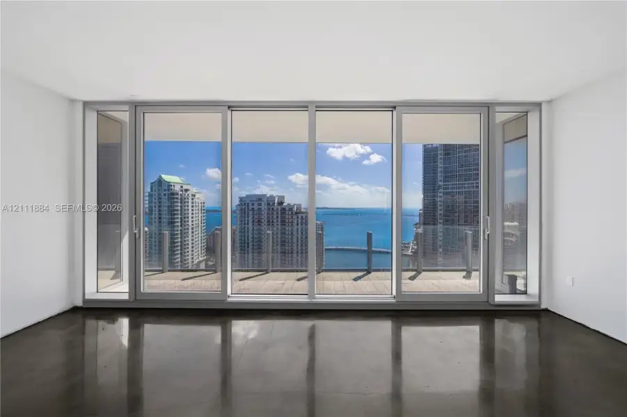 Floor-to-ceiling sliding glass panels, polished concrete flooring, and an expansive outdoor terrace featuring a glass railing with water and city skyline vistas Floor-to-ceiling sliding glass panels, polished concrete flooring, and an expansive outdoor terrace featuring a glass railing with water and city skyline vistas