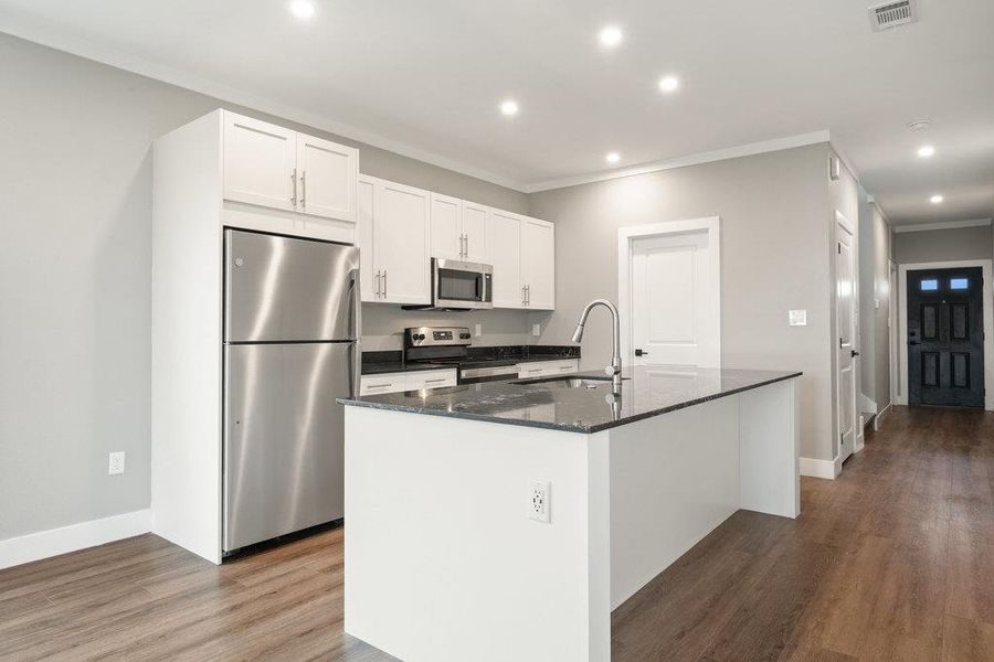 Kitchen featuring appliances with stainless steel finishes, white cabinets, dark quartz countertops, crown molding, and dark wood-type flooring