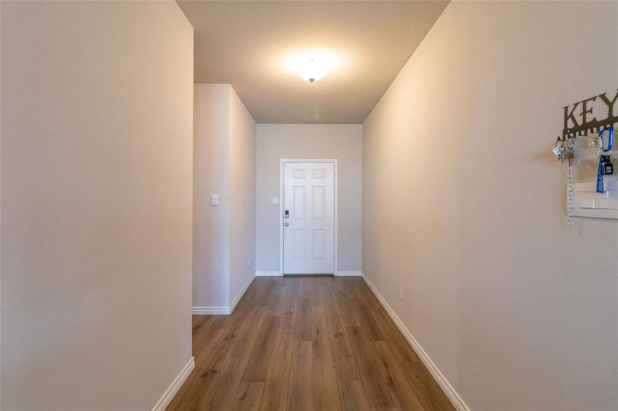 A welcoming entry hall featuring robust hardwood flooring leads to a classic paneled front door.