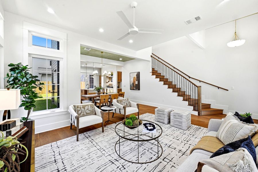 A graceful staircase ascends from a sun-filled living area featuring rich hardwood floors and an open concept layout. A graceful staircase ascends from a sun-filled living area featuring rich hardwood floors and an open concept layout.