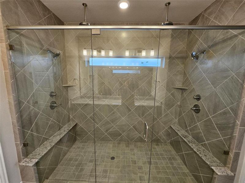 Master bathroom features huge shower with 4 shower heads, 2 granite benches, dropped tile floor, and window