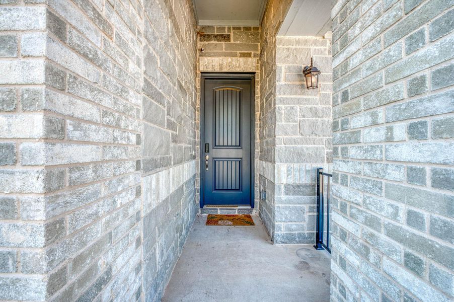 An inviting stone-clad alcove frames the elegant front entry door.