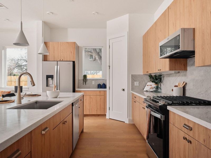 Kitchen with stainless steel appliances, light stone countertops, hanging light fixtures, light wood finished floors, and light wood finish cabinetry