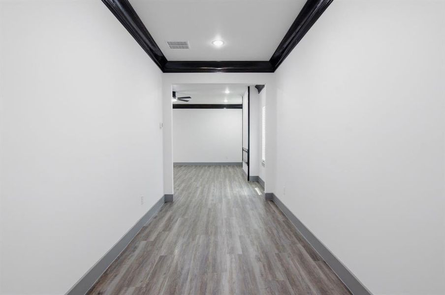 Hallway featuring wood-finish flooring, white walls, dark crown molding, and recessed lighting