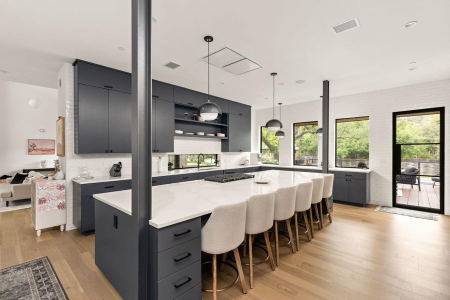 A contemporary kitchen boasts a spacious island with seating, a gas cooktop, and sleek cabinetry, illuminated by chic pendant lighting. A contemporary kitchen boasts a spacious island with seating, a gas cooktop, and sleek cabinetry, illuminated by chic pendant lighting.