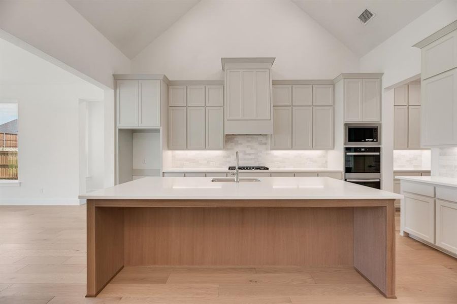 Kitchen with tasteful backsplash, high vaulted ceiling, appliances with stainless steel finishes, white cabinets, and light stone countertops