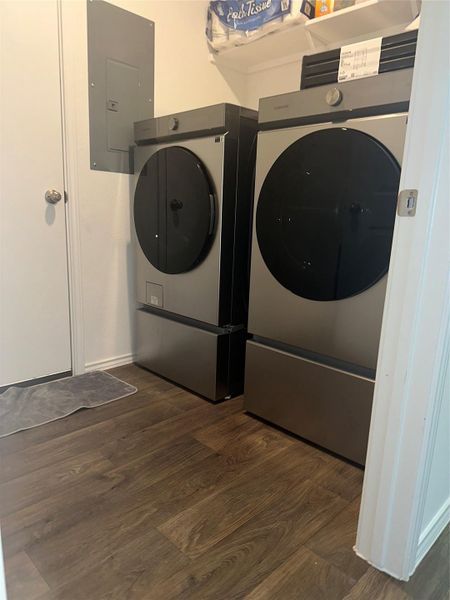 Washroom with dark wood-style flooring, electric panel, and washing machine and clothes dryer