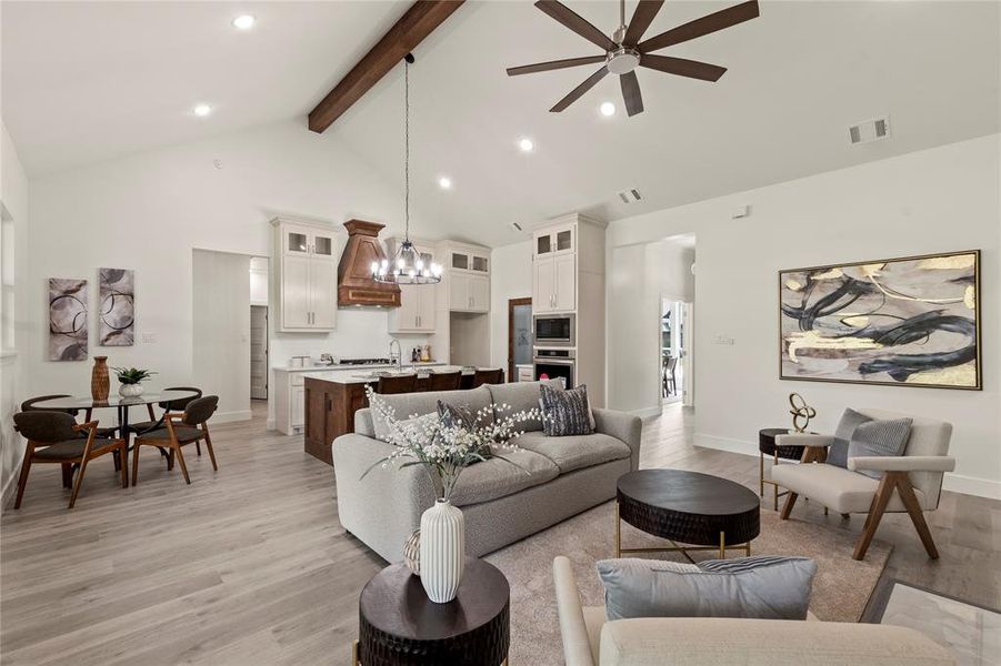 Living area featuring high vaulted ceiling, light wood-type flooring, beamed ceiling, ceiling fan, and baseboards