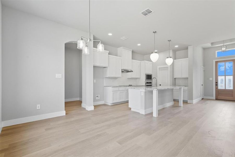 Kitchen featuring arched walkways, a kitchen bar, decorative backsplash, an island with sink, and white cabinets Kitchen featuring arched walkways, a kitchen bar, decorative backsplash, an island with sink, and white cabinets
